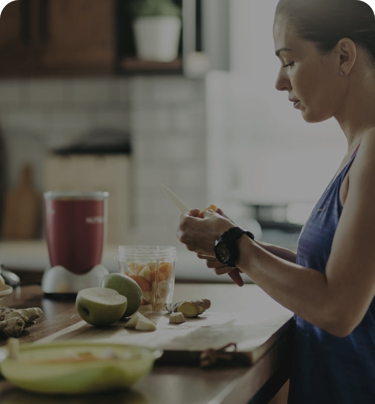 Person cutting fruit in the kitchen for a smoothie with a blender nearby.